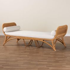 a wicker chaise lounge with white cushions on hardwood flooring in front of a wall