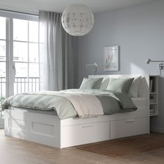 a white bed sitting next to a window in a room with wooden floors and furniture