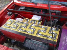 the engine compartment of a red car with batteries in it