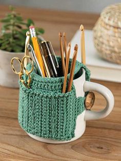 a cup filled with pens and pencils sitting on top of a wooden table next to a potted plant