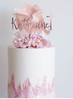 a white cake with pink flowers and a cross on top that says katerhinet