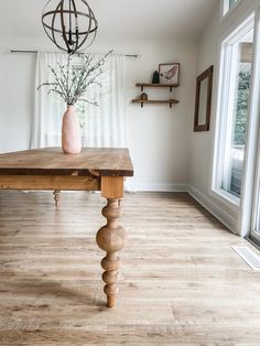 a wooden table sitting in the middle of a living room next to a large window