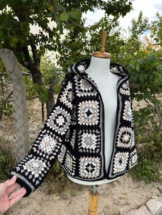 a black and white crocheted jacket is on a mannequin with trees in the background