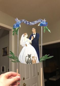 a bride and groom on top of a cake with cats in front of the door