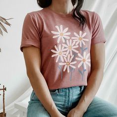 a woman sitting on top of a chair wearing a t - shirt with daisies painted on it