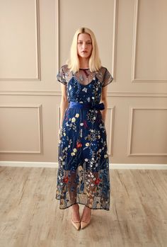 a woman in a blue dress standing on the floor with her hands behind her back