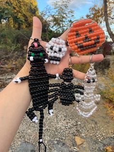 a hand holding two beaded black cats and an orange pumpkin on it's palm