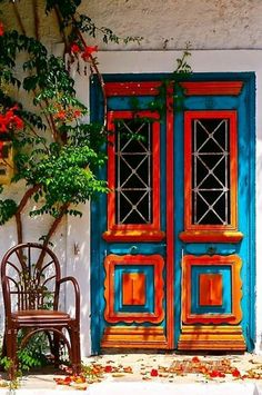 a wooden chair sitting in front of a blue and yellow door with red flowers on it