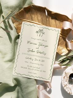 the wedding stationery is laid out on top of a leafy green cloth, next to a pair of black stones