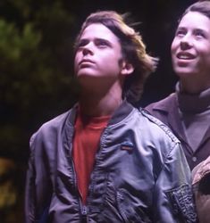 two young men standing next to each other in front of some trees and one has his eyes closed