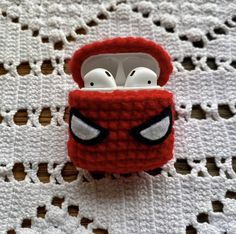 an earphone case made to look like a deadpool character is sitting on top of a crocheted doily