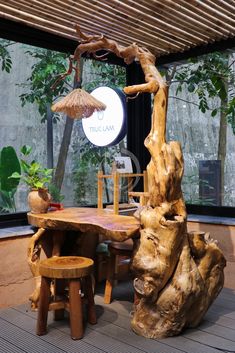 a wooden table and two stools in front of a tree stump with an umbrella over it