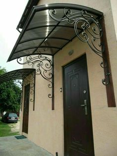 a brown door is next to a white building with a black metal awning over it