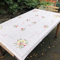 a table cloth with flowers on it sitting next to a wooden bench and shrubbery