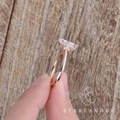 a hand holding a diamond ring on top of a wooden table