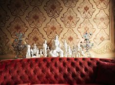 a red couch sitting in front of a wallpapered room with figurines on it