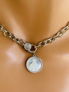 This is a beautiful 14k white gold filled chain choker necklace with mother of pearl etched miraculous Mary pendant hanging from front pave lobster clasp. These beautiful pendant measures 18 mm. features the miraculous image of MARY surrounded with pavé crystals. Necklace chain links measure 10 X7MM. Clasp sits at front that holds pendant. This necklace is also available in 14k gold filled.  Model has a small neck and is wearing a 15 inch length. Please choose your desired length. Comes in a gift box ready to present. Please choose the length and primary color. Elegant Sterling Silver Necklace With Miraculous Medal, Elegant Charm Necklace With Lobster Clasp And Medallion, Elegant Medallion Charm Necklace With Lobster Clasp, Elegant Miraculous Medal Necklace, Silver Necklace With Miraculous Medal For Wedding, Elegant Round Miraculous Medal Jewelry, Elegant Miraculous Medal Jewelry For Gift, White Gold Pendant Charm Necklace With Lobster Clasp, Elegant Miraculous Medal Jewelry Gift