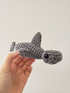 a hand holding a crocheted toy that looks like a small gray shark with it's mouth open