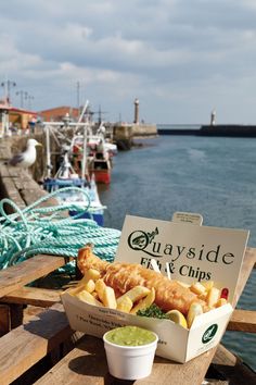 a fish and chips box sitting on top of a wooden table next to the water