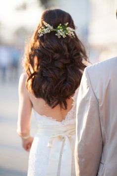 a bride and groom walking together down the street with their back to the camera, looking at each other