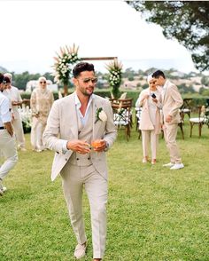 a man in a suit and tie walking through the grass with other men behind him