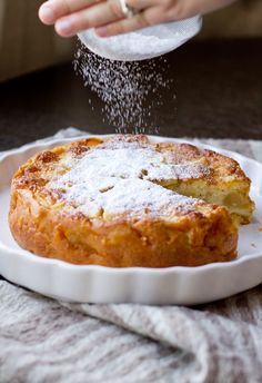 someone sprinkles sugar on top of a baked pastry in a white dish