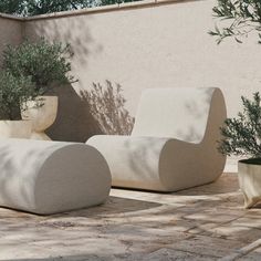 an outdoor seating area with potted plants on the ground and concrete benches in front of a stucco wall