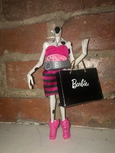 a mannequin holding a black bag and wearing pink boots with the word barbie written on it