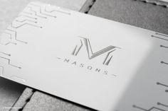 a metal business card sitting on top of a gray piece of paper with the word masons printed on it