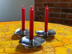 two red candles sitting on top of each other in front of a yellow table cloth