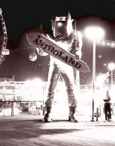 a black and white photo of a man holding a skateboard in front of a ferris wheel