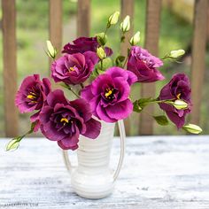 purple flowers are in a white vase on a table