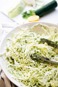 a white plate topped with coleslaw and cucumbers next to other vegetables