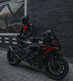 a motorcycle parked next to a brick wall with a man in black and red riding on it