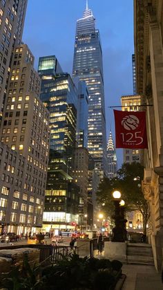 the skyscrapers are lit up at night in new york city, with people walking on the sidewalk