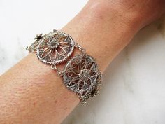 "This is a lovely vintage filigree bracelet. Made of sterling silver, the circle links all have a center raised flower inside a sunburst/snowflake design. The links are 1\" in diameter. The length of the bracelet is 8 1/4\" long. The large spring ring clasp is secure. Total weight of the bracelet is 16.2dwt/25.1grams. This is a vintage, previously owned bracelet. Therefore, light wear can be expected. There is no visible damage." Metal Bracelets With Intricate Design, Antique Silver Bracelets With Intricate Design, Ornate Hallmarked Sterling Silver Bracelet, Vintage Sterling Silver Bracelet With Intricate Design, Vintage Filigree Round Bracelets, Antique Filigree Round Bracelets, Round Solitaire Diamond Necklace, Filigree Bracelet, Vintage Sterling Silver Charms