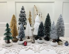 there are many small christmas trees on the table and one is white with gold trimmings