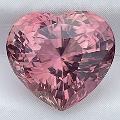 a pink heart shaped diamond sitting on top of a white surface