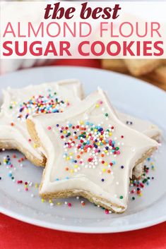 some cookies with icing and sprinkles are on a white plate next to a red table cloth