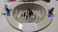 two figurines sitting on top of a toilet bowl with clothes pins attached to it