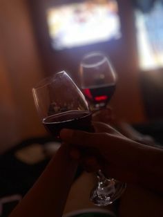 two people toasting with red wine in front of a tv