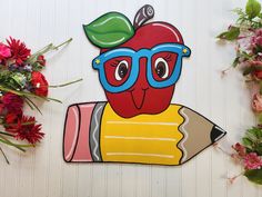 an apple wearing glasses and holding a pencil in front of some flowers on the wall