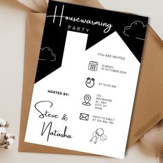 a black and white housewarming party card on top of a brown envelope next to flowers