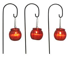 three red glass vases are hanging from black metal stands with hooks on each side