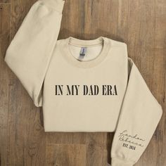 Celebrate Father's Day in style with our "In My Dad Era" personalized sweatshirt, featuring Dad Est 2024 and your kids' names elegantly printed on the sleeve. This custom Dad sweatshirt is the perfect heartfelt gift that combines comfort and a personal touch, making it an unforgettable addition to any dad's wardrobe🤍 ♥ PRODUCT DETAILS & SIZING This pre-shrunk, classic fit sweatshirt is made with air-jet spun yarn for a soft feel and reduced pilling. ♥ Pre-shrunk ♥ Classic fit with no center cre Customizable Long Sleeve Sweatshirt For Father's Day, Father's Day Cotton Sweatshirt With Name Print, Personalized Crew Neck Sweatshirt In Relaxed Fit, Personalized Relaxed Fit Crew Neck Sweatshirt, Custom Text Cotton Hoodie With Crew Neck, Custom Text Cotton Crew Neck Hoodie, Kids Names, Shirt Store, Workout Sweatshirt