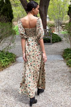 a woman in a long dress is standing near a tree