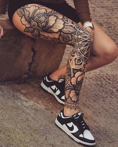 a woman sitting on top of a stone wall wearing black and white flowers tattoo leggings