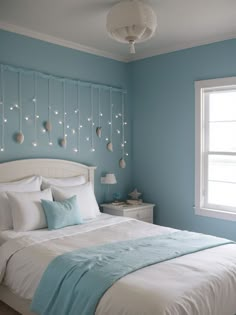 a bedroom with blue walls, white bedding and string lights on the headboard