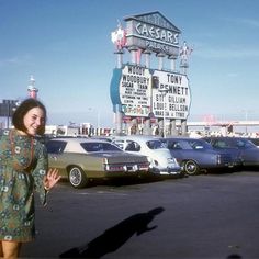 a woman is standing in front of cars at a car dealership with a large sign behind her