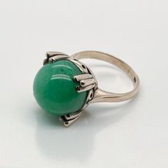 A very fine 14k gold and jade bead Art Deco style ring.  With a large jadeite bead prong set in a 14k gold architectural setting.  Simply a wonderful ring!  Date: Early to Mid 20th Century  Overall Condition: It is in overall good, as-pictured, used estate condition. There is mottling and a fine natural fissure visible to the top of the stone, as well as some very fine & light surface scratches and other signs of expected light wear consistent with age.  Fineness: Marked 14K for gold fineness. Formal Cabochon Chrysoprase Jewelry, Elegant Emerald Jade Ring With Cabochon, Modernist Round Cabochon Jewelry, Formal Round Jade Jewelry, Elegant Domed Emerald Ring, Elegant Green Gemstone Dome Ring, Art Deco Jade Jewelry For Formal Occasions, Elegant Green Dome Ring, Formal Art Deco Jade Jewelry